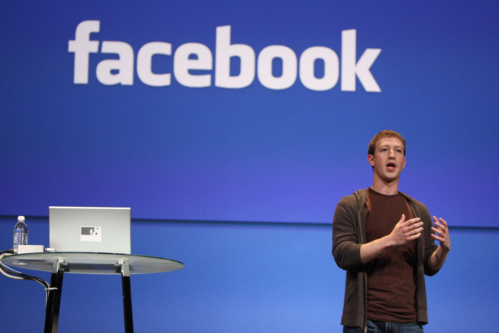 Mark Zuckerberg berdiri di panggung dengan logo Facebook.