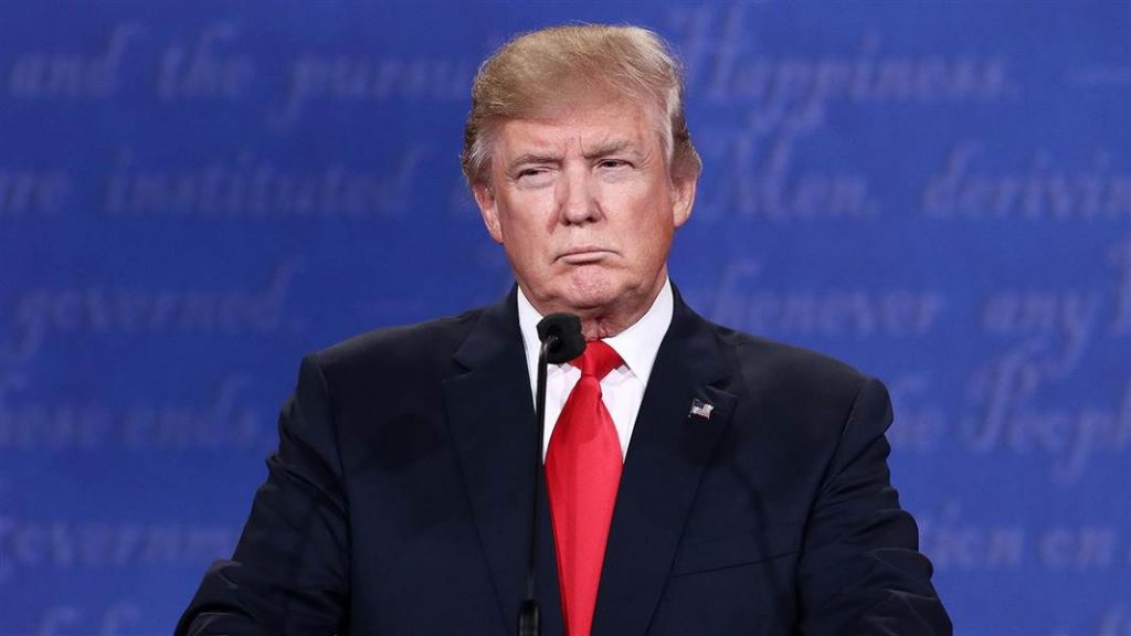 Donald Trump berdiri di podium dengan dasi merah.
