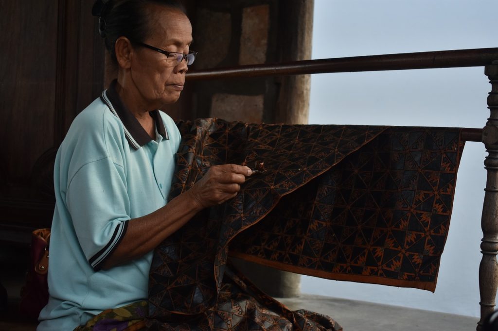 Perempuan mengerjakan kain batik di dalam ruangan.