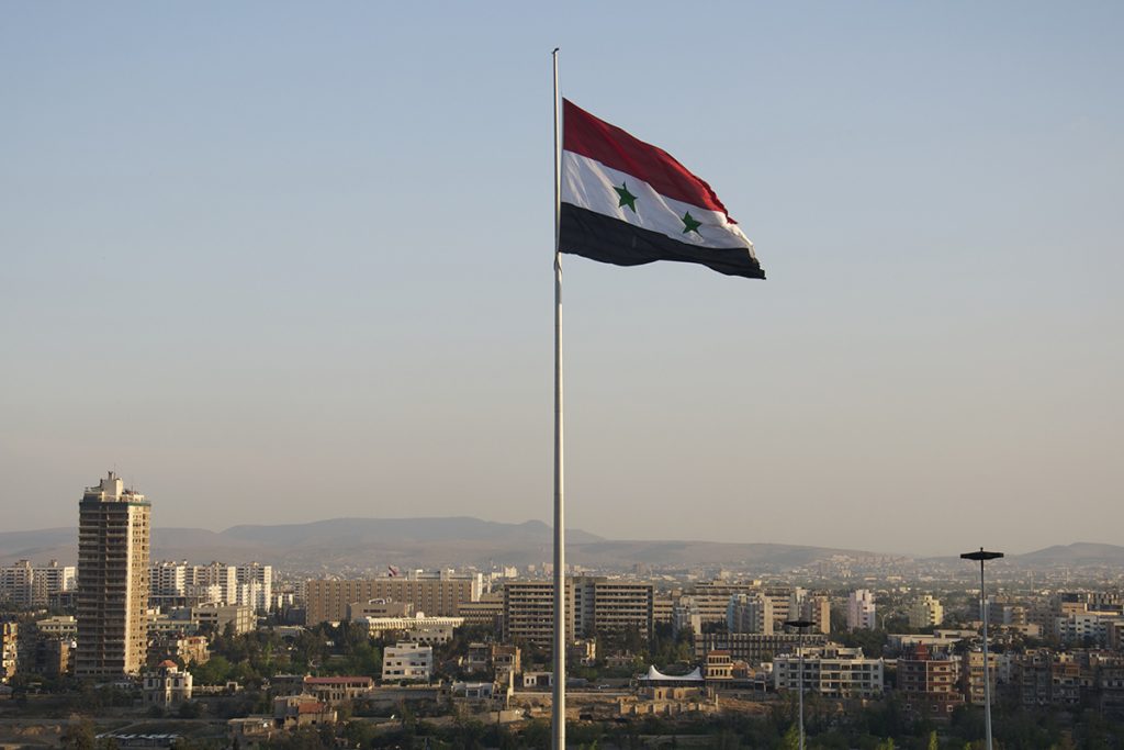 Bendera Suriah berkibar di atas pemandangan Damaskus.