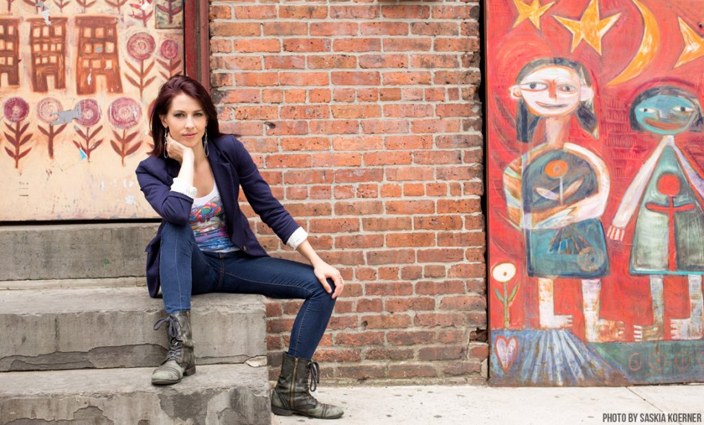 Abby Martin duduk pada tangga di depan dinding berlukis.