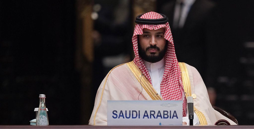 Mohammed bin Salman duduk di belakang papan Saudi Arabia.