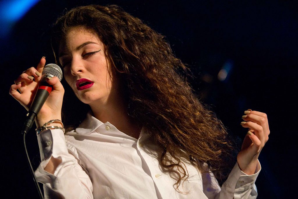 Lorde bernyanyi sambil memegang mikrofon.